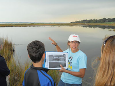 Wenley Ferguson, director of habitat restoration for Save The Bay, shows an aerial photo of the Barrington Beach salt marsh from 2012 showing the degree of impoundment to the marsh, and degradation caused by standing water.